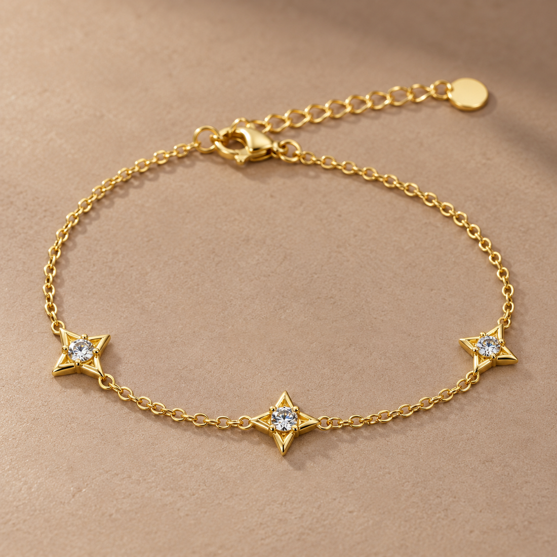 Gold-tone 316L chain bracelet with three four-point star motifs each set with a clear round stone, laid flat with a lobster clasp and extender chain