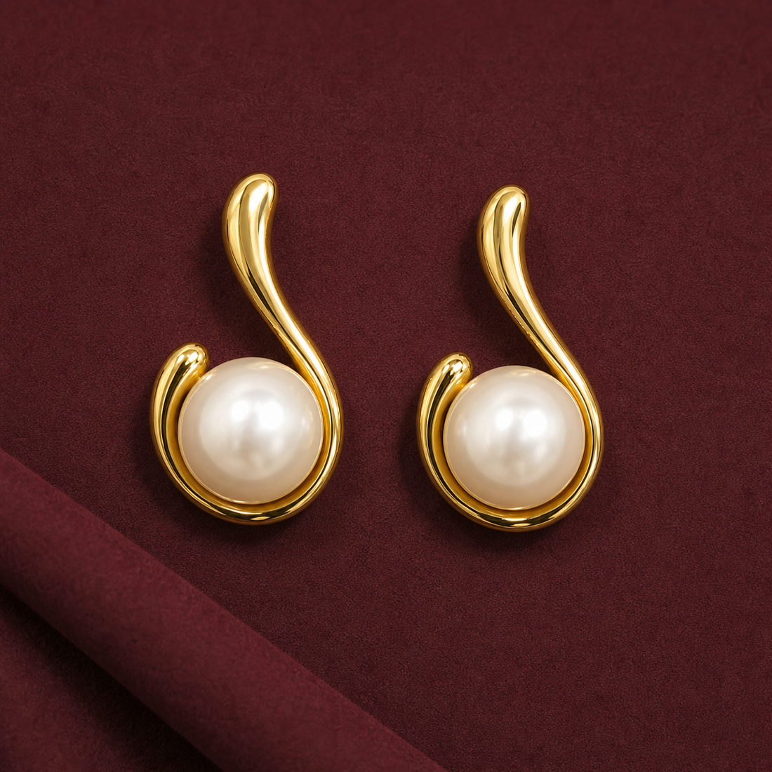 Gold-tone 304 stainless steel stud earrings with a swirl-shaped curved frame holding a white pearl bead, shown as a pair on a maroon background