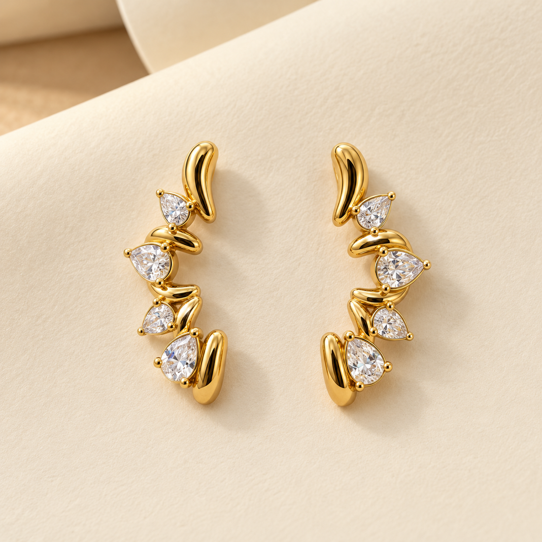 Gold-tone 316L stainless steel earrings with curved gold bars and four pear-cut clear stones set in a vertical row, a pair on a cream background