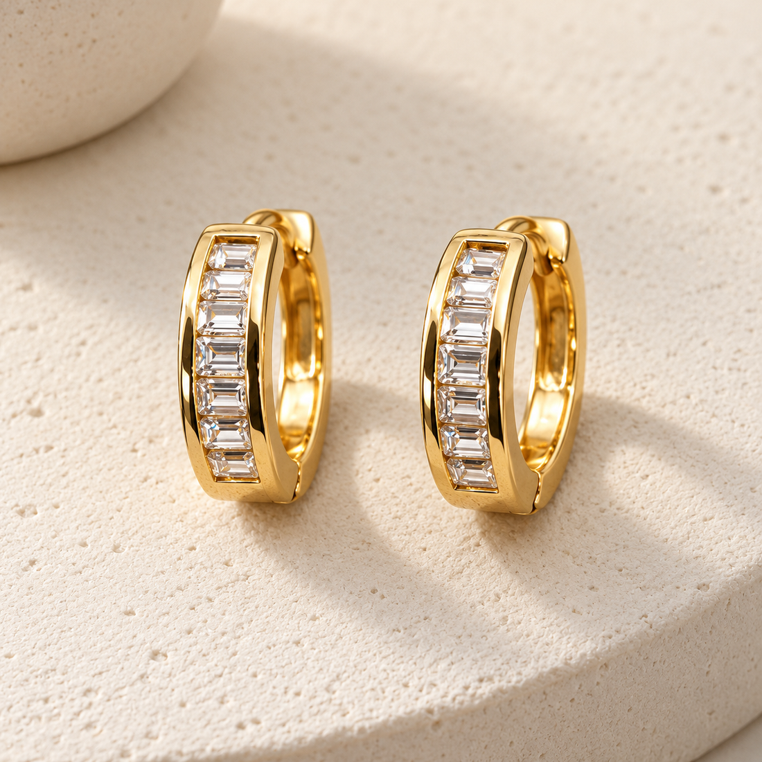 Gold-tone 316L stainless steel huggie hoop earrings, a pair, with a row of baguette-cut clear stones set along the front of each hoop
