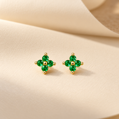 Gold-tone 316L stainless steel stud earrings with four green stones in a cross cluster and a gold-tone centre bead, shown as a pair on a cream fabric background