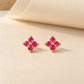 Gold-tone 316L stainless steel stud earrings with four pink-red round stones forming a flower motif, shown as a pair on a cream surface