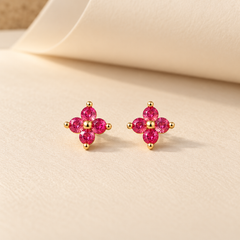 Gold-tone 316L stainless steel stud earrings with four pink-red round stones forming a flower motif, shown as a pair on a cream surface