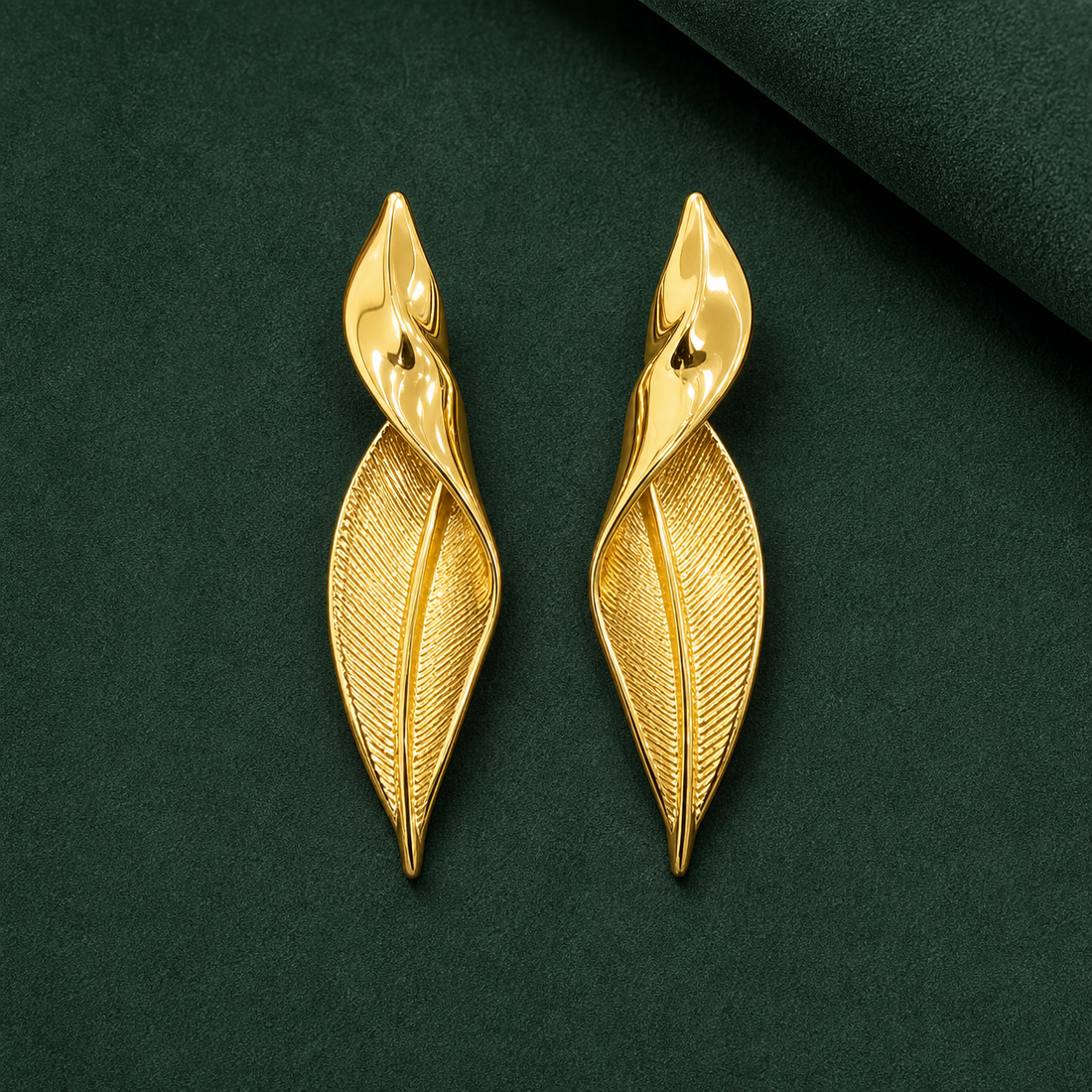 Gold-tone 304 stainless steel drop earrings shaped as twisted leaves with a smooth top and a fine-lined underside, a pair on a dark green background