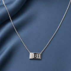 Silver-tone 316L stainless steel necklace with a thin cable chain and a rectangular plate engraved with 11:11, lying on blue fabric