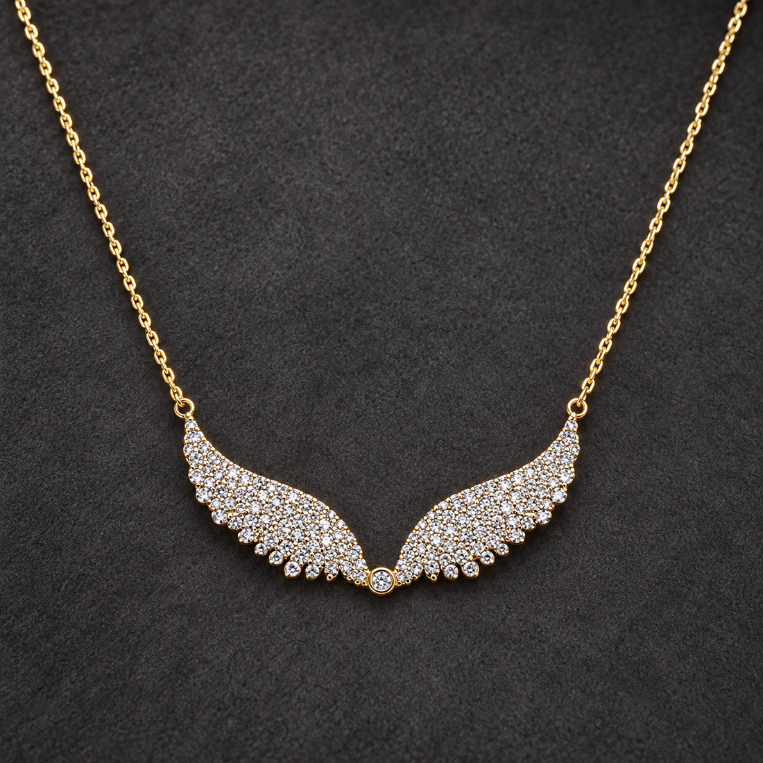 Gold-tone 316L stainless steel necklace with a fine cable chain and a pendant of two wings set with clear stones, laid flat on a dark surface