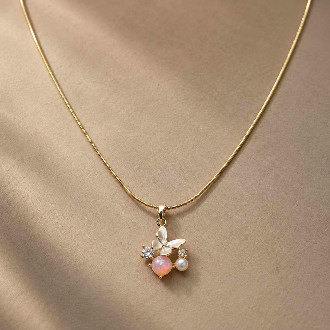 Gold-tone 316L stainless steel snake chain necklace with a butterfly pendant set with an opal-look stone, a pearl and two clear stones, worn on a neck
