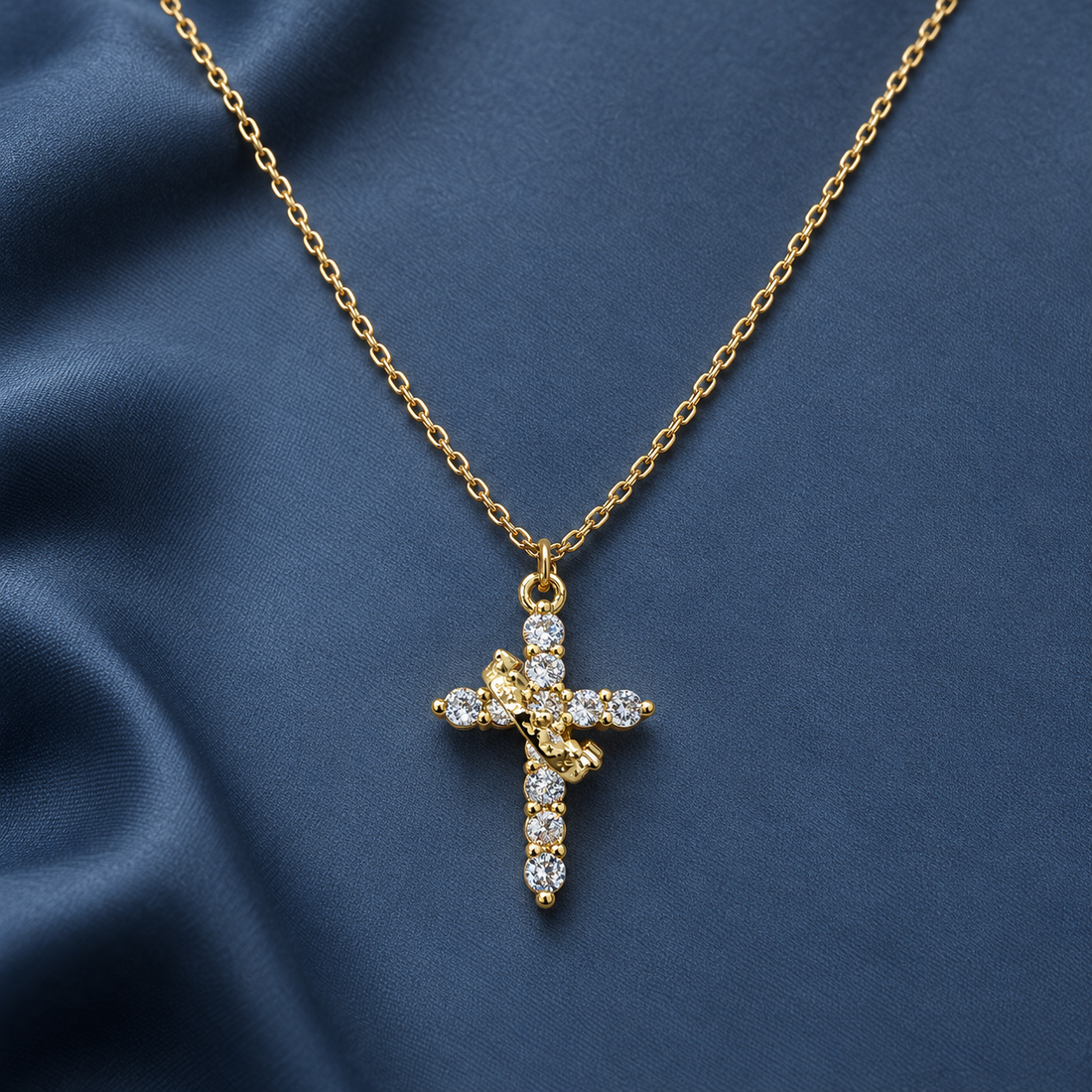 Gold-tone 304 stainless steel cross pendant necklace with clear stones set along the cross and a fine cable chain, worn on a blue satin backdrop