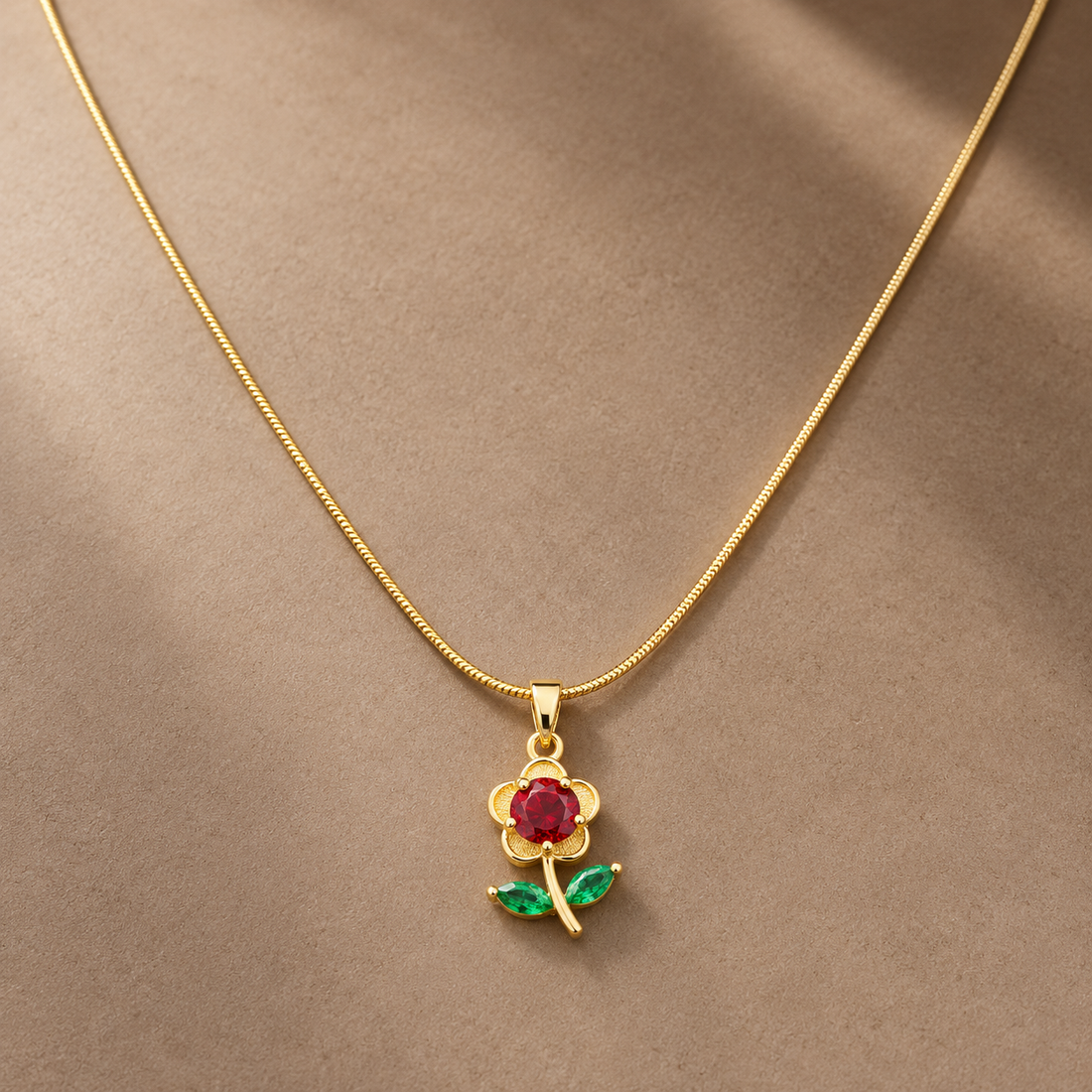 Gold-tone 316L stainless steel flower pendant necklace with a red round stone centre and green marquise leaves on a thin snake chain, worn at the neck