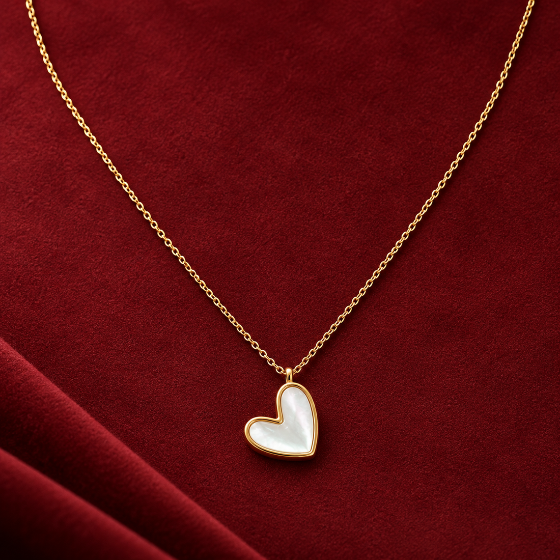 Gold-tone 316L chain necklace with a heart-shaped mother-of-pearl pendant in a gold-tone bezel, displayed on a red velvet cloth