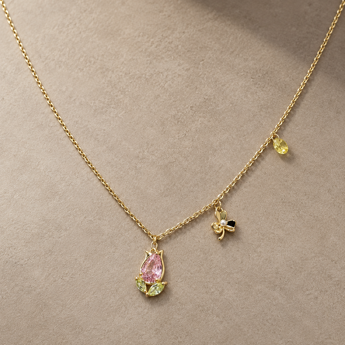 Gold-tone 316L stainless steel necklace with a pink pear stone tulip pendant, green leaf stones and a bow charm