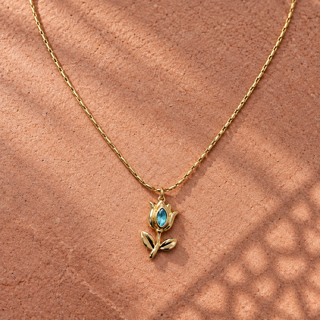 Gold-tone 304 stainless steel tulip pendant necklace with a blue marquise stone in the bloom and two leaves, on a fine chain, shown lying flat