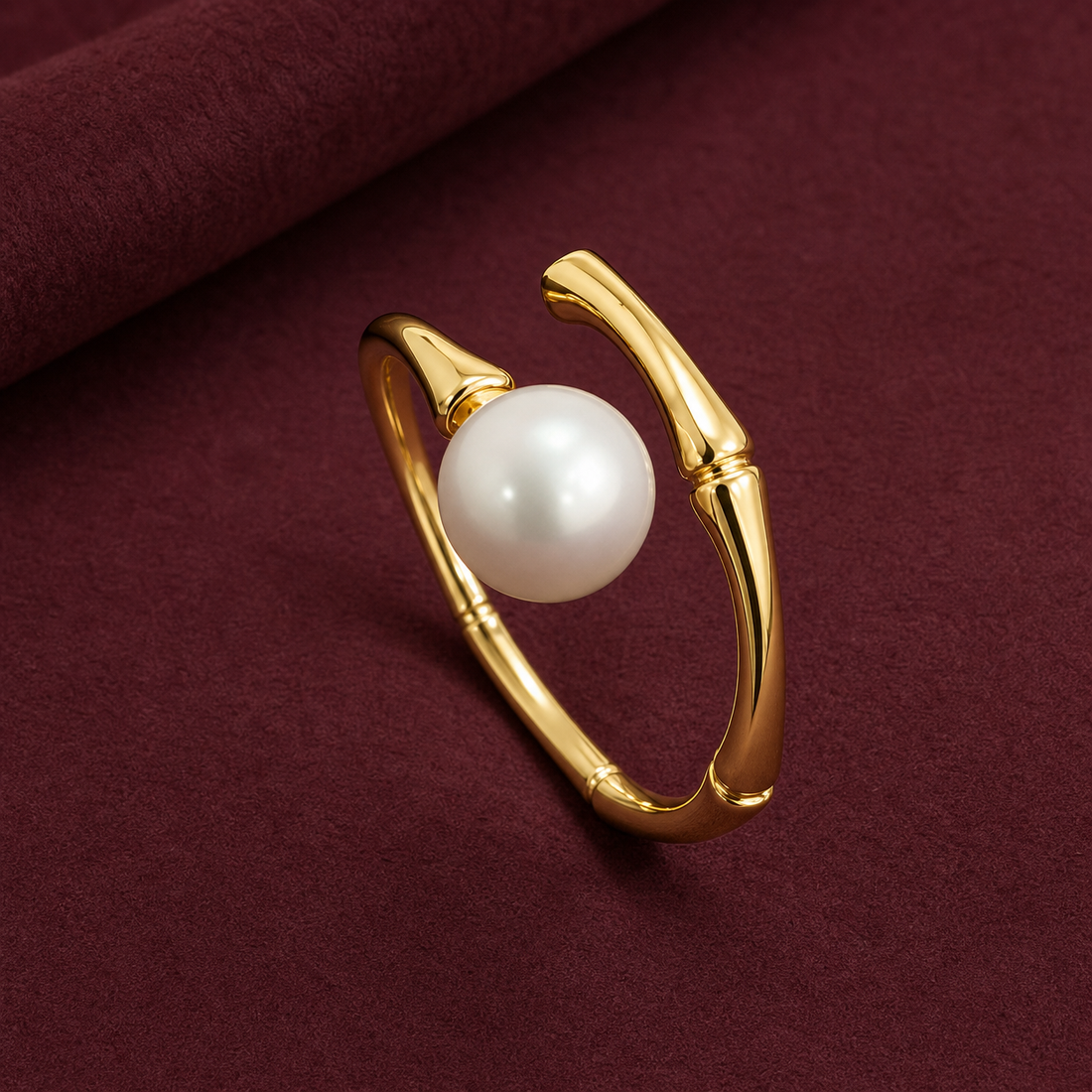 Gold-tone 316L stainless steel open ring with a bamboo-segment band and a large white pearl set at the front, shown on a burgundy surface