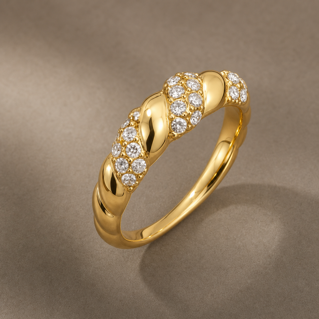 Gold-tone 316L ring with a twisted rope band and clusters of clear stones along the top, shown from an angled view