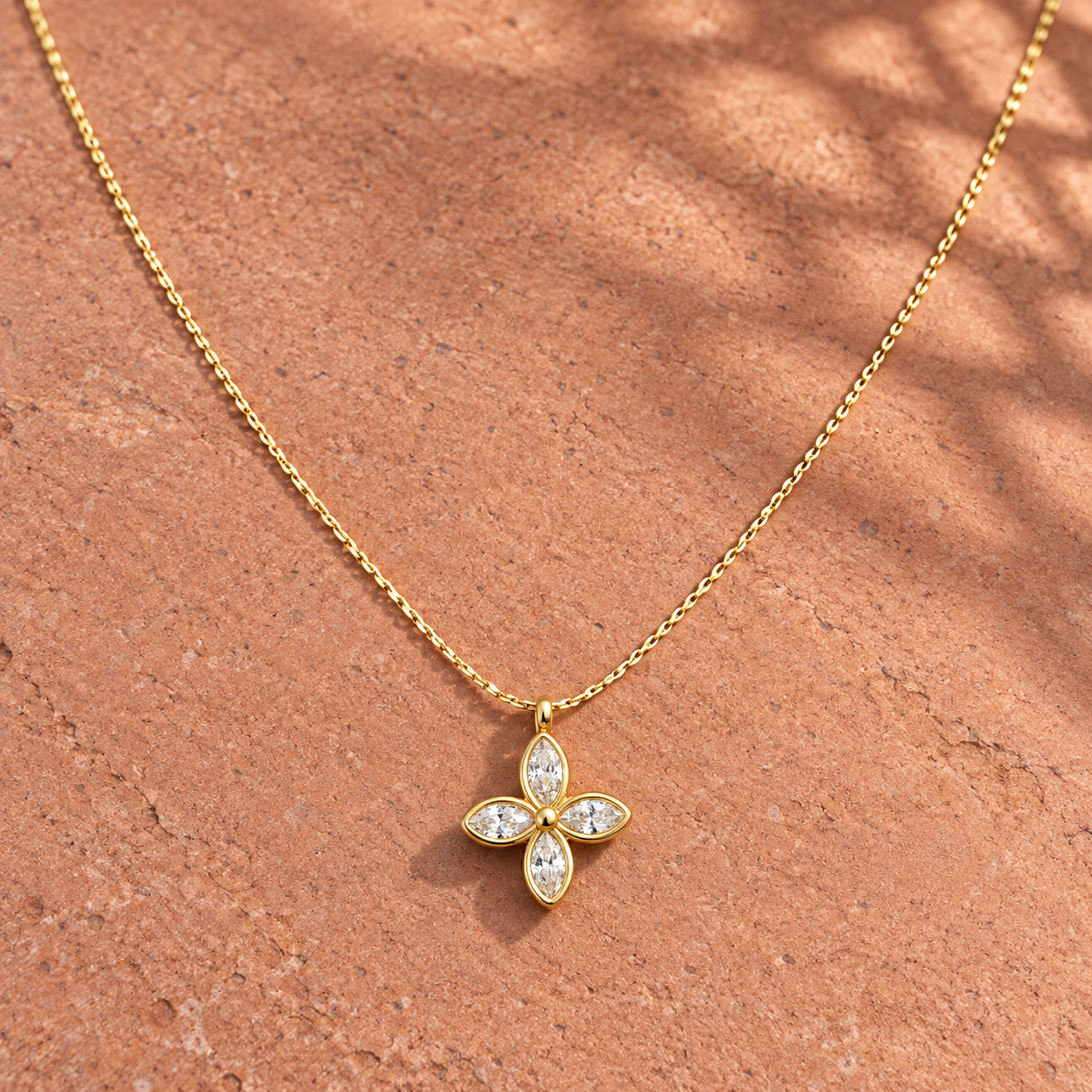 Gold-tone 316L stainless steel necklace with a cable chain and a four-petal flower pendant set with clear marquise stones, lying on a stone surface