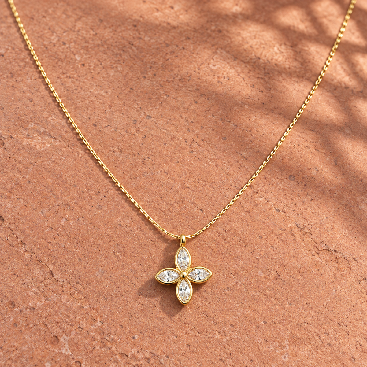 Gold-tone 316L stainless steel necklace with a cable chain and a four-petal flower pendant set with clear marquise stones, lying on a stone surface