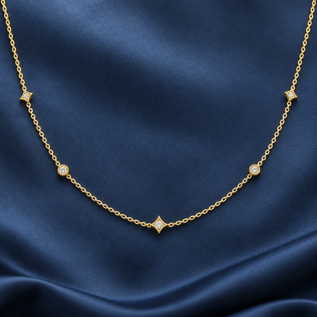 Gold-tone 316L stainless steel necklace with a fine cable chain and five star-shaped and round stone-set stations, laid flat on navy fabric