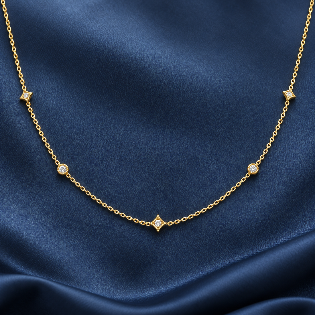 Gold-tone 316L stainless steel necklace with a fine cable chain and five star-shaped and round stone-set stations, laid flat on navy fabric