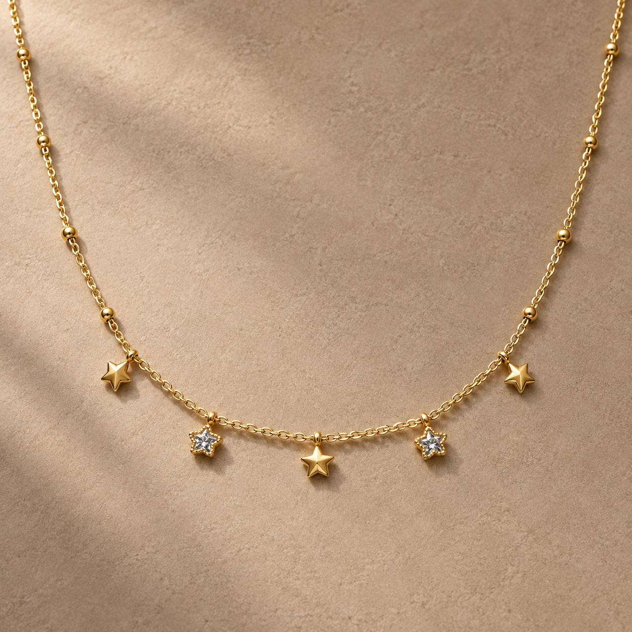 Gold-tone 316L stainless steel necklace with a fine chain, bead spacers and five star charms, two of them set with clear stones, worn at the neck