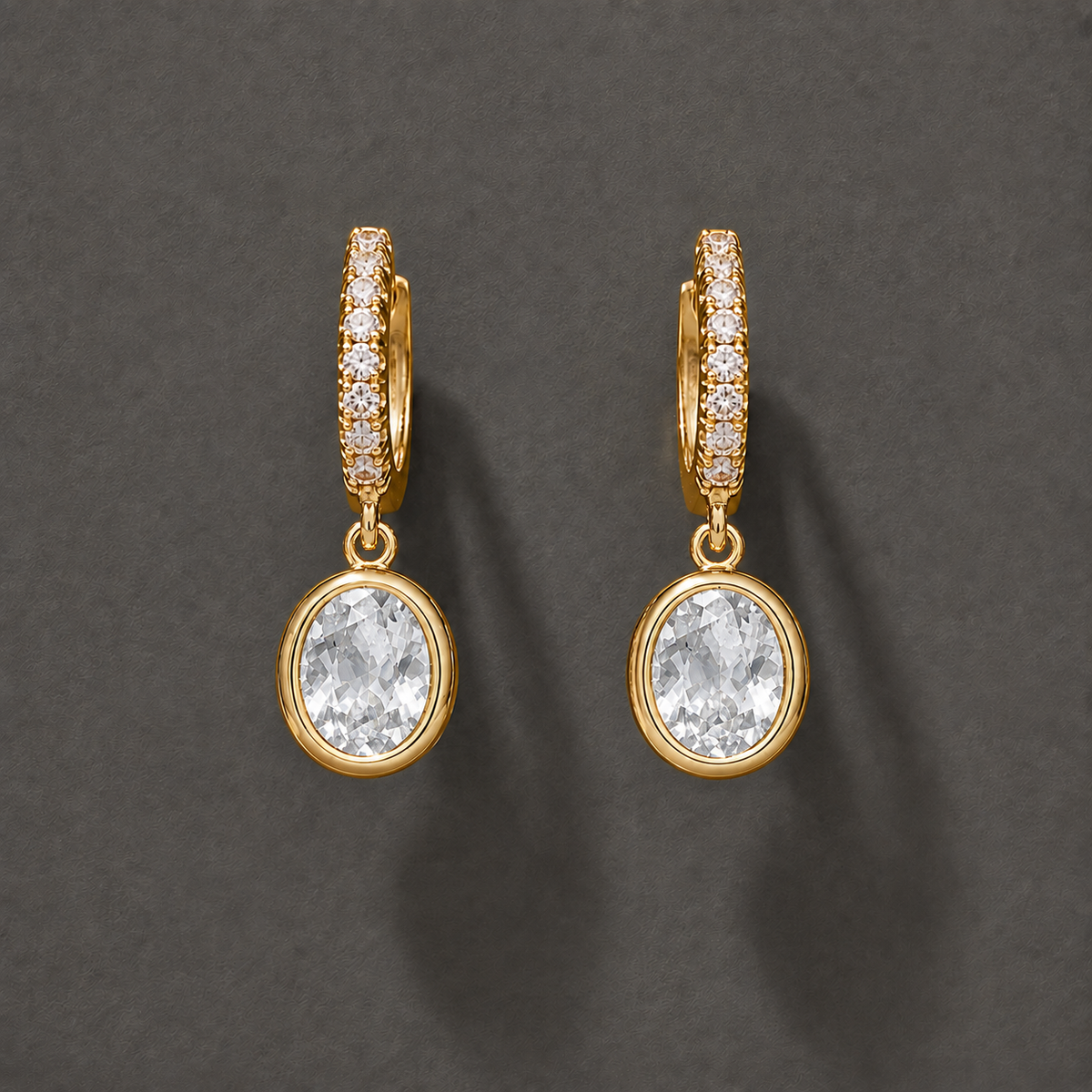 Gold-tone 304 stainless steel huggie hoop earrings with pavé crystals and an oval clear stone drop, a pair on a grey background