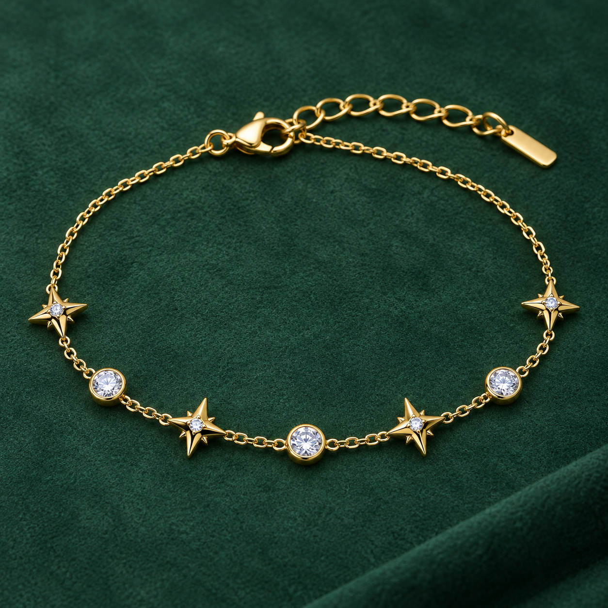 Gold-tone 316L stainless steel chain bracelet with alternating four-point star and round clear stone charms, flat view on green fabric