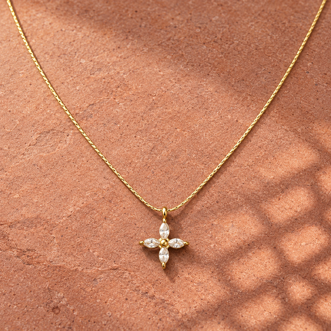 Gold-tone 316L stainless steel necklace with a fine chain and a cross pendant set with four marquise stones, lying on a stone surface