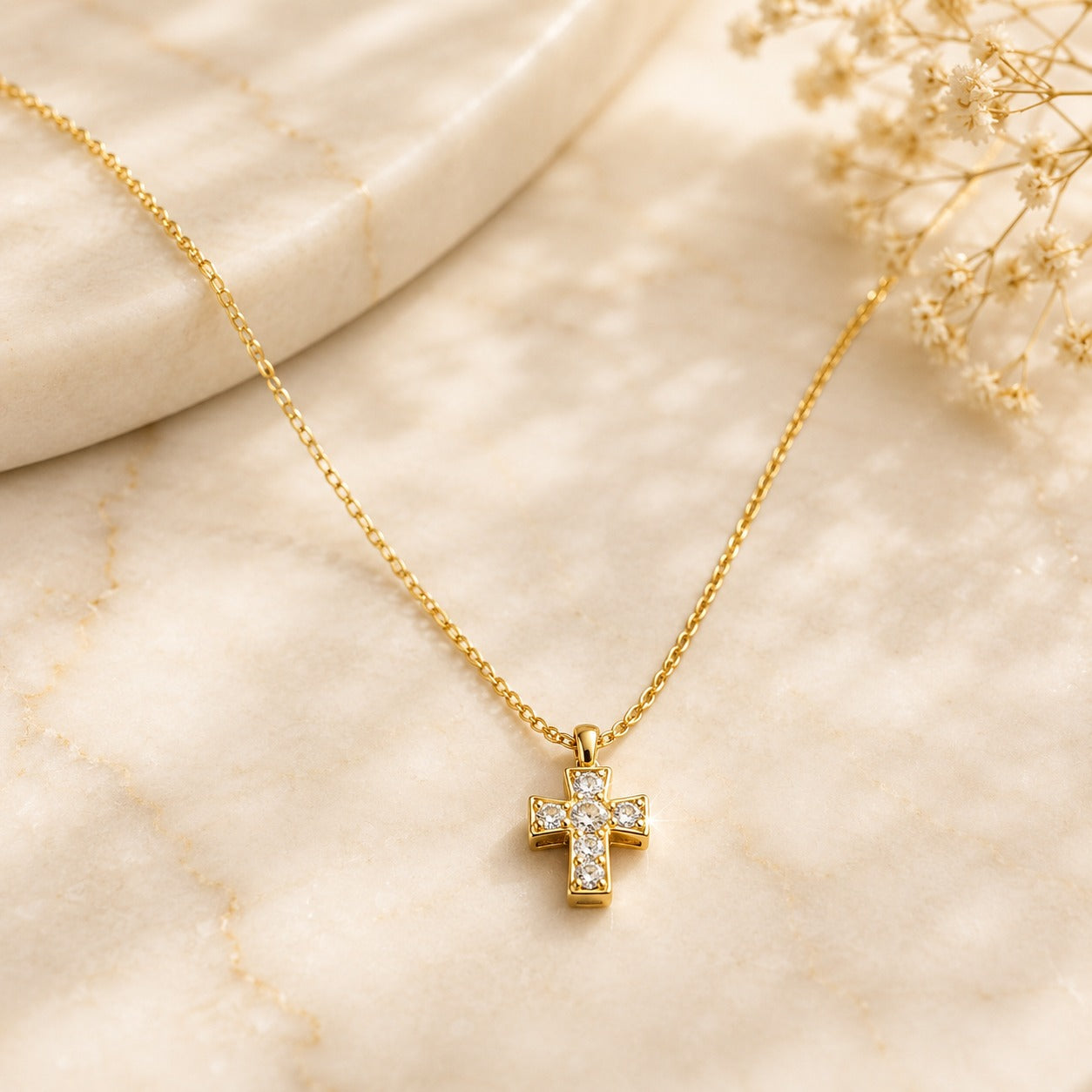 Gold-tone 316L stainless steel chain necklace with a small cross pendant set with clear stones, laid flat on a marble surface