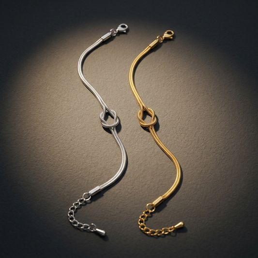 Silver-tone and gold-tone 316L stainless steel snake chain bracelets with a knot motif, lying flat on a dark surface