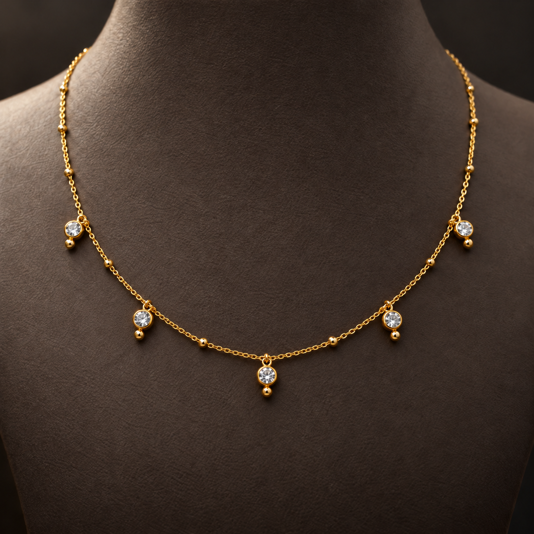 Gold-tone 316L stainless steel necklace with a fine chain, small ball beads and five clear crystal drops, worn on a dark display bust