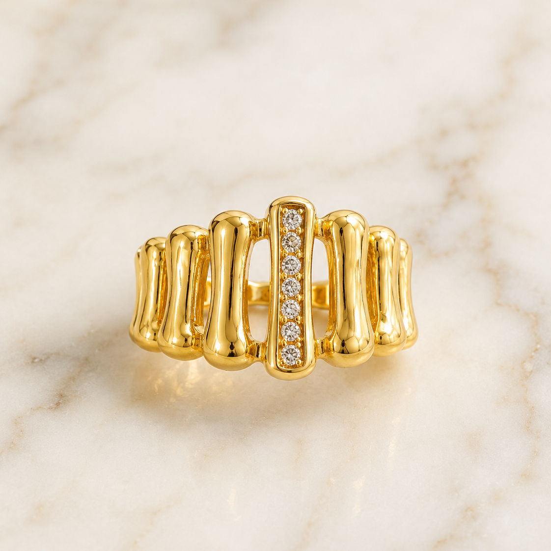 One earring, though its ear fitting is not visible and is partly obscured; no post, hook or back can be resolved. Yellow-gold-tone metal with a high-polish finish. The piece is a rigid, articulated-looking band of rounded vertical ribbed segments, each a smooth solid-metal lobe, joined by narrow open gaps. At the centre a raised rectangular bar holds seven round brilliant-cut clear faceted stones in a vertical channel-style line, graduated only slightly, each the same small size relative to the rib width.