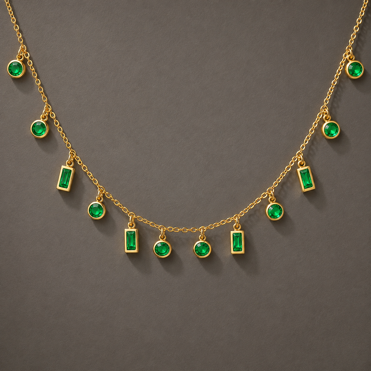 Gold chain necklace with multiple dangling emerald-cut green gemstone charms and round green gemstone accents, displayed against a dark gray background.