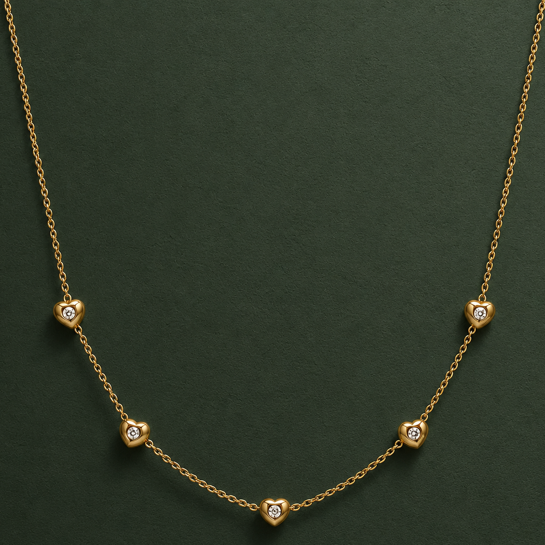 A delicate gold chain necklace featuring five small, alternating heart and diamond-shaped gold pendants, each set with a tiny clear stone, displayed on a dark green textured background.