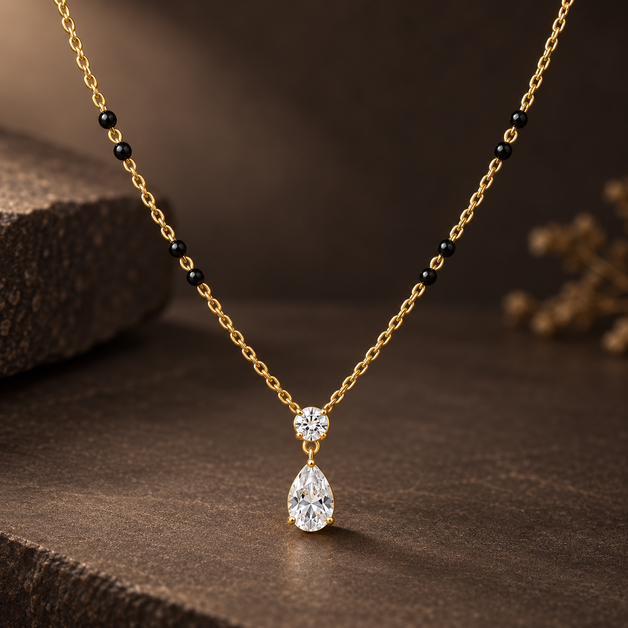 Gold-tone 316L stainless steel mangalsutra necklace with black beads on a chain and a pear-cut white stone pendant below a round stone