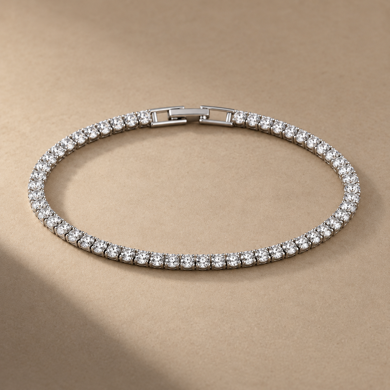 Silver-tone brass tennis bracelet with a row of clear round stones in claw settings and a box clasp, laid flat on a beige surface