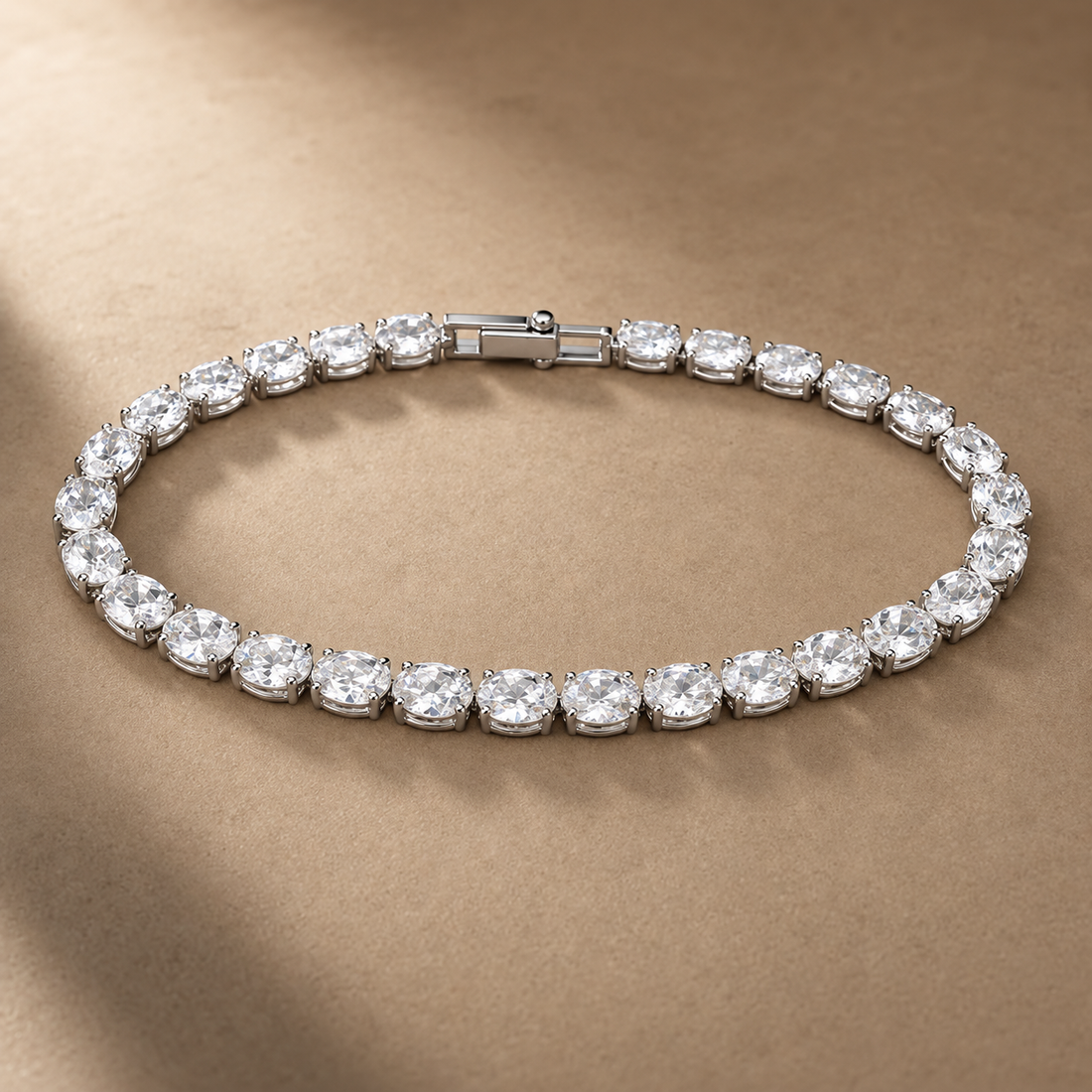 Silver-tone brass tennis bracelet with a row of oval clear stones in claw settings and a box clasp, laid flat on a beige surface