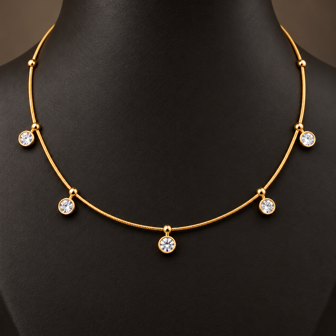 Gold-tone 304 necklace with a thin snake chain and five round clear stones in bezel settings hanging from it, worn on a mannequin neck, close view