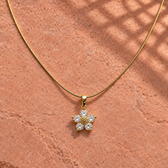 Gold-tone 316L stainless steel necklace with a snake chain and a flower pendant set with five clear stones, lying on a stone surface