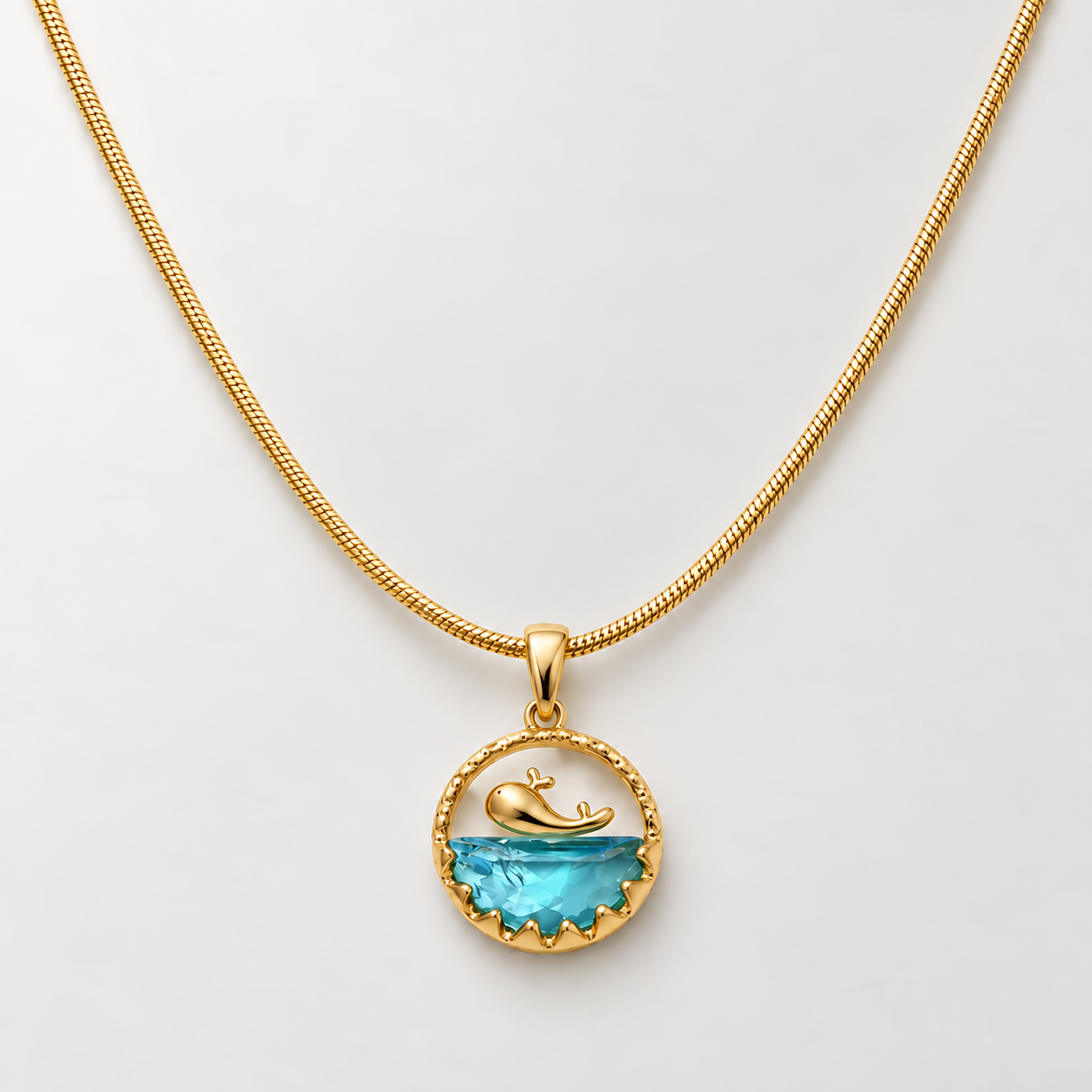 Gold-tone 316L stainless steel pendant necklace with a gold whale motif above a blue faceted stone in a scalloped round frame, on a snake chain