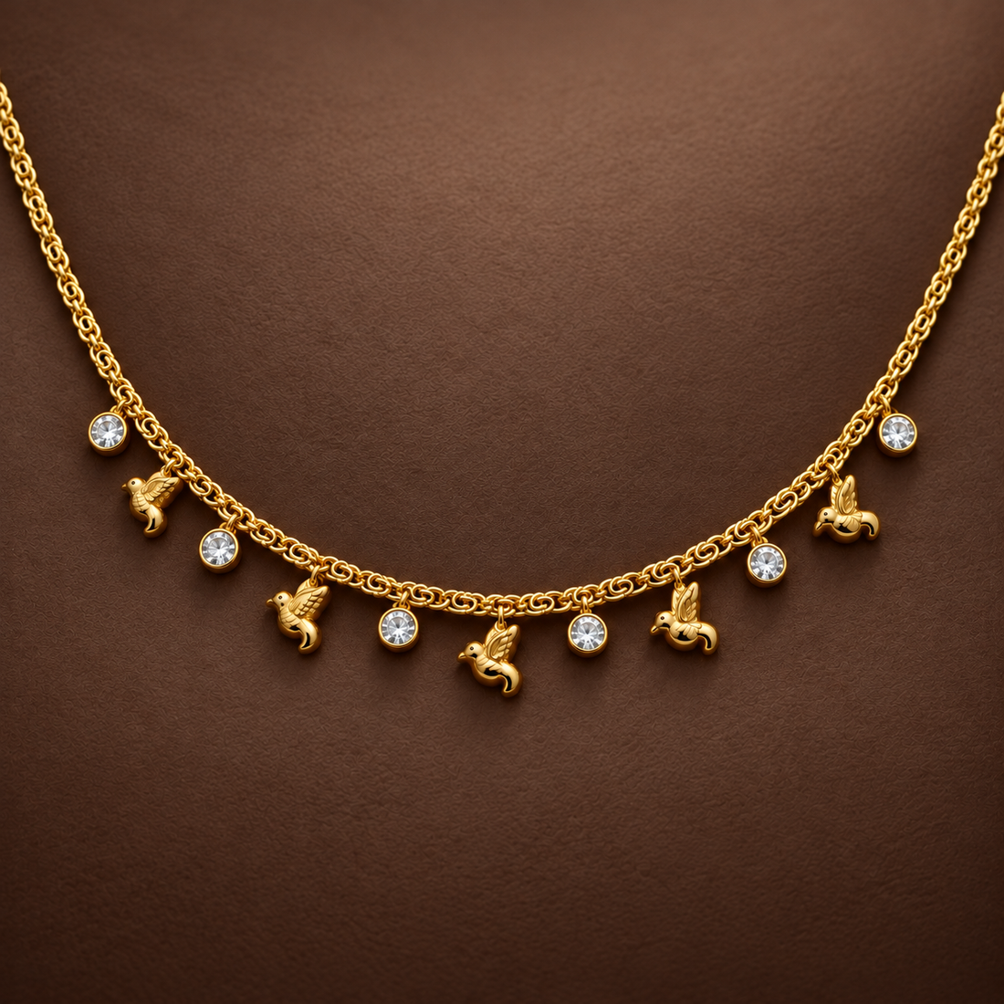 Gold-tone 316L stainless steel necklace with a link chain and dangling bird and round crystal charms, shown on a dark brown backdrop