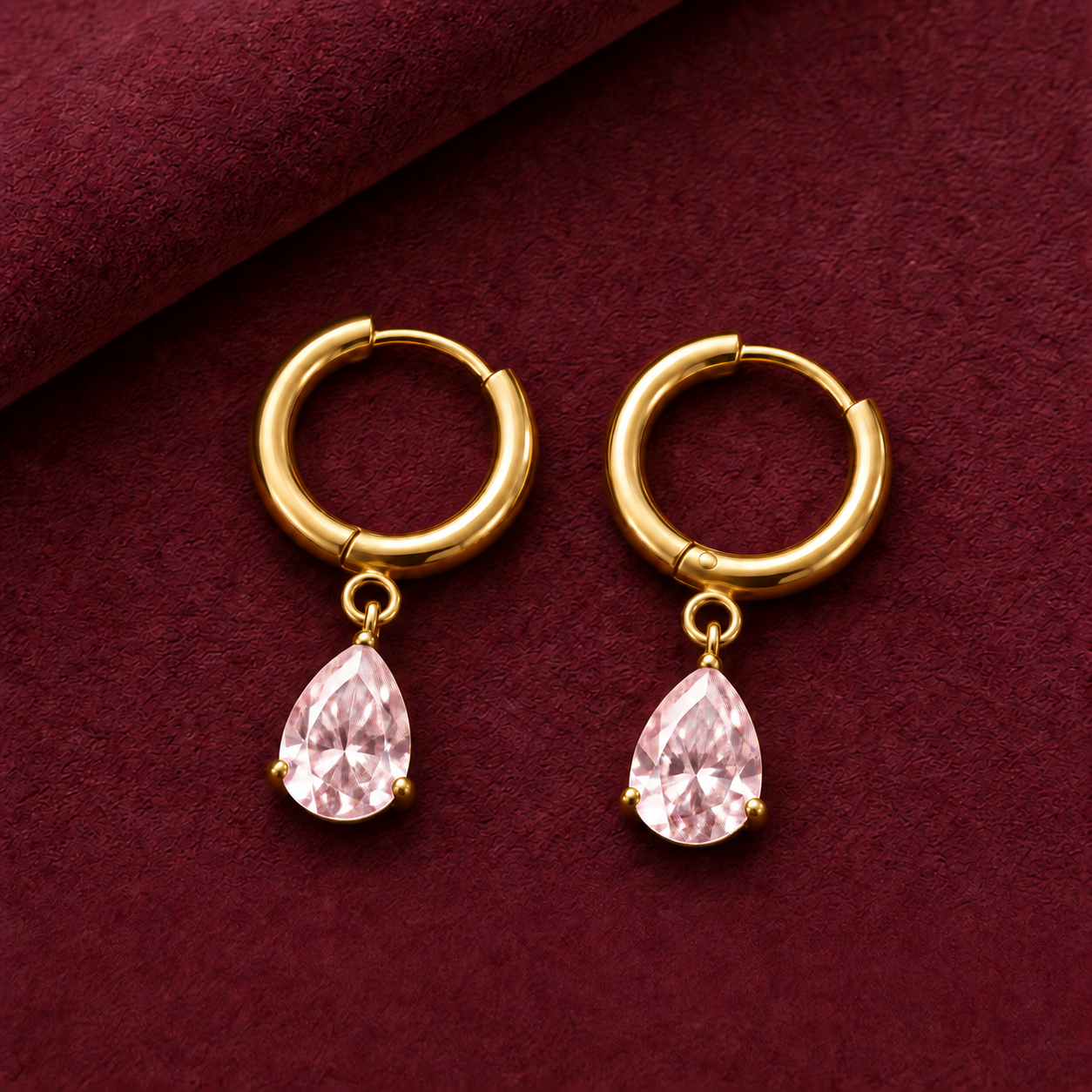 Gold-tone 316L stainless steel hoop earrings with a pear-cut pink crystal drop hanging from each hoop, shown as a pair