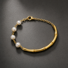 A single wrist-worn chain bracelet in polished gold-toned metal. Construction is a single strand of two joined sections: one section is a rigid-curve run of bamboo-style cylindrical tube segments (about six segments with raised ring joints), and the other is a fine cable chain of small oval links carrying five round white pearls, each drilled and linked between short chain sections. The full chain run is roughly twelve times the width of one pearl, the largest component.