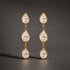 Two ear-worn earrings of one design in yellow-gold-tone metal with a polished finish. Each earring carries three pear-shaped clear faceted stones in matching gold-tone bezel-style mounts, linked vertically by small jump rings so the three sections articulate and swing independently. Stones decrease slightly in size downward, though the uppermost stone reads slightly smaller than the middle one. Overall drop is roughly four times the width of the widest stone.