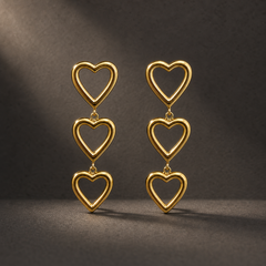 Two ear-worn earrings of one design in yellow-gold-toned metal with a polished finish. Each is a three-tier drop of open-frame solid-metal heart motifs, roughly equal in size, the top heart carrying the fitting and each lower heart suspended from the one above by small jump-ring links, giving three articulated sections; overall drop is approximately three times the width of the widest heart.