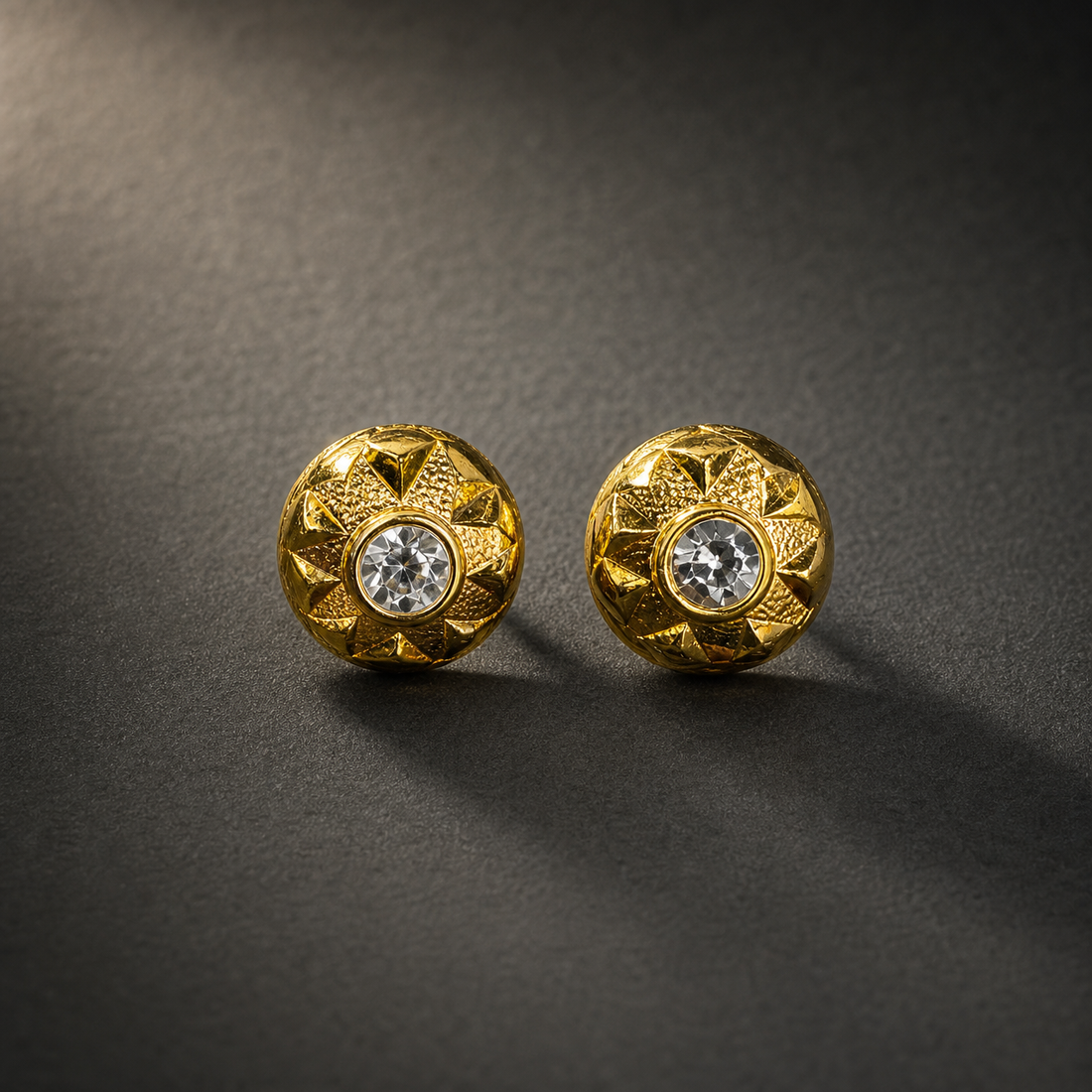 Two ear-worn stud earrings of one design, in yellow-gold-coloured metal with a polished and textured finish. Each is a single rigid domed disc, roughly as deep as it is wide, with no articulation or hanging sections. The fitting is a post and back; the posts are partly obscured, so length and gauge cannot be confirmed.