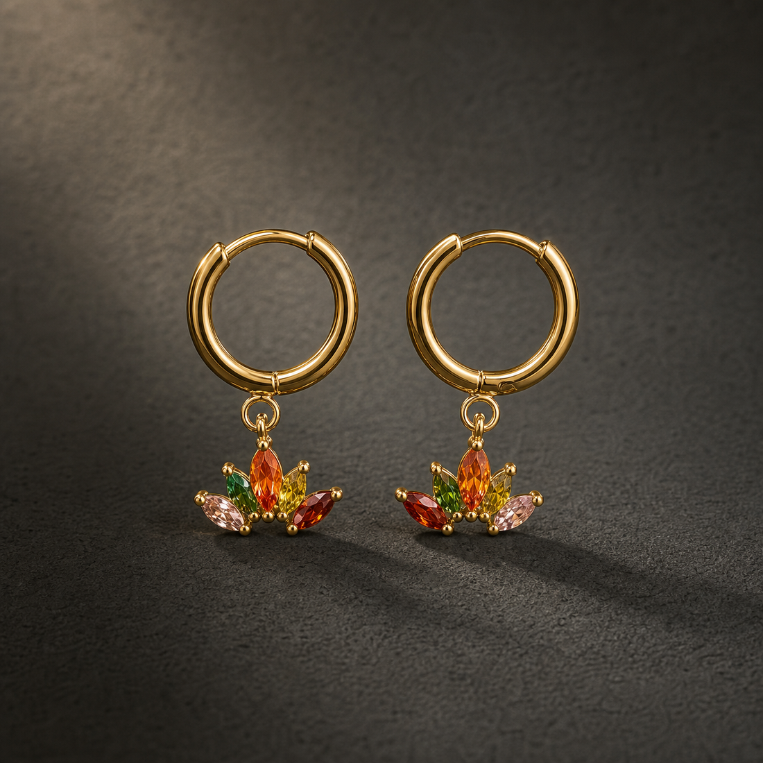 Two earrings of one design, each a small yellow-gold-tone hoop with a polished finish and a huggie-hinge hoop closure; the hoop wire is slender gauge. From each hoop a single charm section hangs on a small jump ring, giving two articulated sections per earring, hinging at the jump ring. Overall drop is approximately one-and-a-half times the hoop diameter. Each charm is a solid-metal fan mounting a cluster of marquise-cut elements in red, orange, green and pink-to-clear tones, individually prong-set.