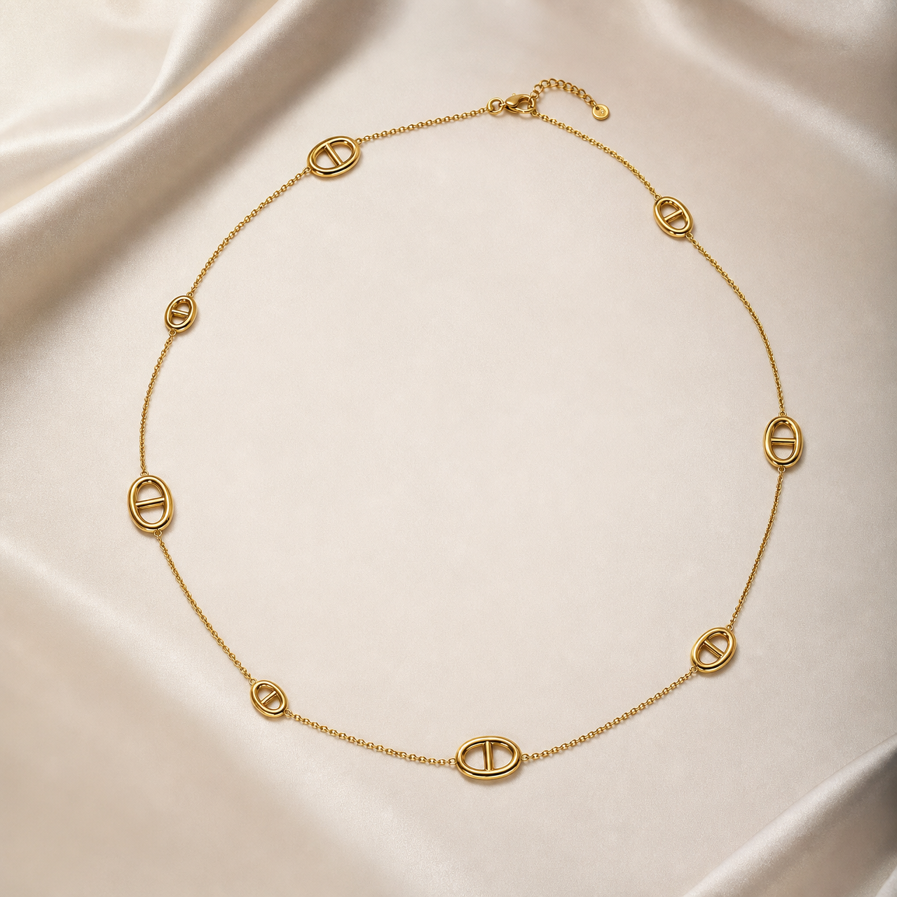 One single-strand station necklace in yellow-gold-toned metal with a polished finish, laid open in a rough square. The chain is a fine, small-gauge round-link cable chain carrying 8 fixed oval solid-metal stations at irregular spacings; each station is an open oval ring with a single straight bar spanning its centre, the bar integral to the oval rather than set or mounted, and there are no stones, beads or charms.