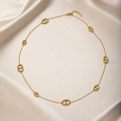 One single-strand station necklace in yellow-gold-toned metal with a polished finish, laid open in a rough square. The chain is a fine, small-gauge round-link cable chain carrying 8 fixed oval solid-metal stations at irregular spacings; each station is an open oval ring with a single straight bar spanning its centre, the bar integral to the oval rather than set or mounted, and there are no stones, beads or charms.