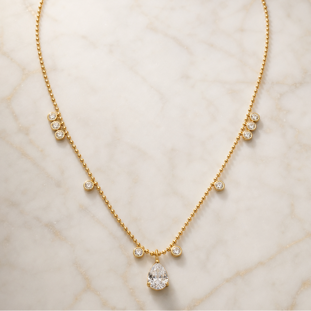 One necklace in yellow-gold-coloured metal with a polished finish, built as a single fine ball/bead chain of small uniform spherical links. From the clasp end (clasp itself not visible, presumably at the chain's far ends) moving toward the centre, each side carries the same sequence: a tight vertical cluster of three small round clear faceted stones in individual bezel settings fixed to the chain, then a gap of plain chain, then one single round bezel-set clear stone, then more plain chain, then one