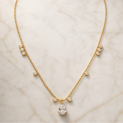 One necklace in yellow-gold-coloured metal with a polished finish, built as a single fine ball/bead chain of small uniform spherical links. From the clasp end (clasp itself not visible, presumably at the chain's far ends) moving toward the centre, each side carries the same sequence: a tight vertical cluster of three small round clear faceted stones in individual bezel settings fixed to the chain, then a gap of plain chain, then one single round bezel-set clear stone, then more plain chain, then one