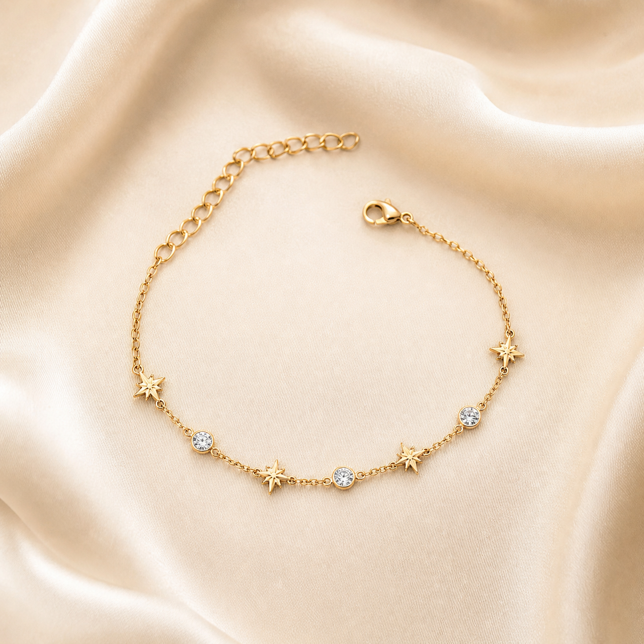 One bracelet, a single-strand flexible chain in yellow-gold-coloured polished metal. The chain is a fine cable link of small, even gauge running its full length with no branches. From the lobster-clasp end toward the opposite end, the decorative stations read: a solid-metal eight-pointed starburst with raised rays, then a round clear faceted element in a smooth gold-coloured bezel, then a second identical starburst, a second clear bezel-set round stone, a third starburst, a third clear bezel-set round